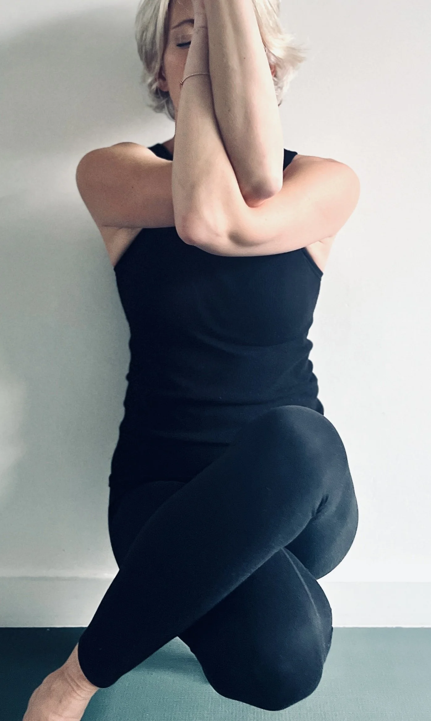 Vrouw in een rustige yogahouding tegen een lichte achtergrond, gericht op balans en ontspanning.