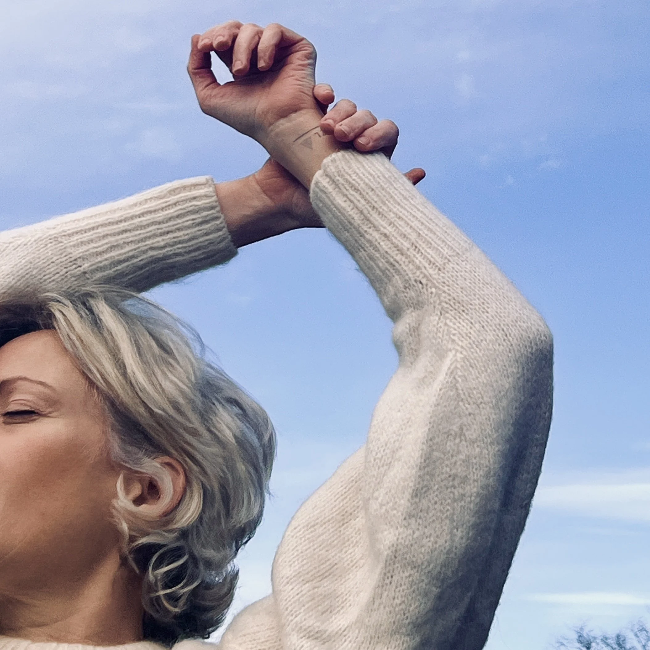 Vrouw met gesloten ogen die haar gezicht naar het licht richt, met armen omhoog in de buitenlucht.