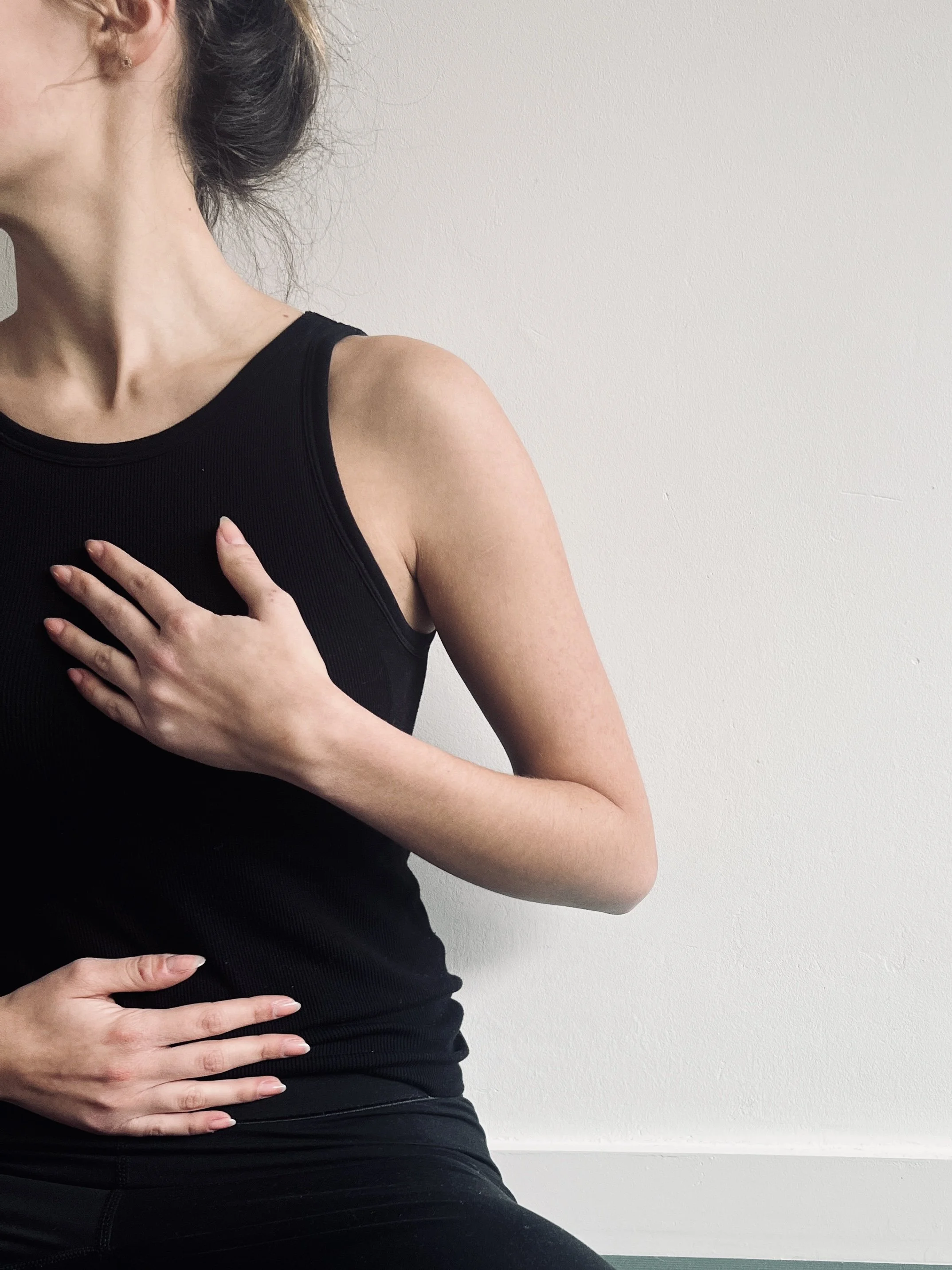 Persoon die met één hand op de borst en één hand op de buik staat, gericht op ademhaling en lichaamsbewustzijn.