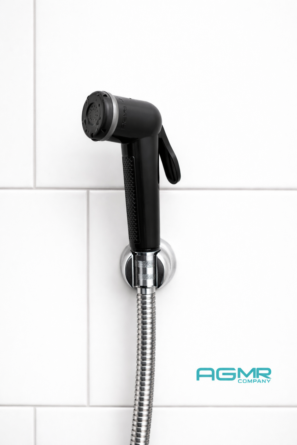 Black showerhead mounted on a white tiled wall with a flexible metallic hose, featuring the logo 'AGMR Company' in the bottom right corner.