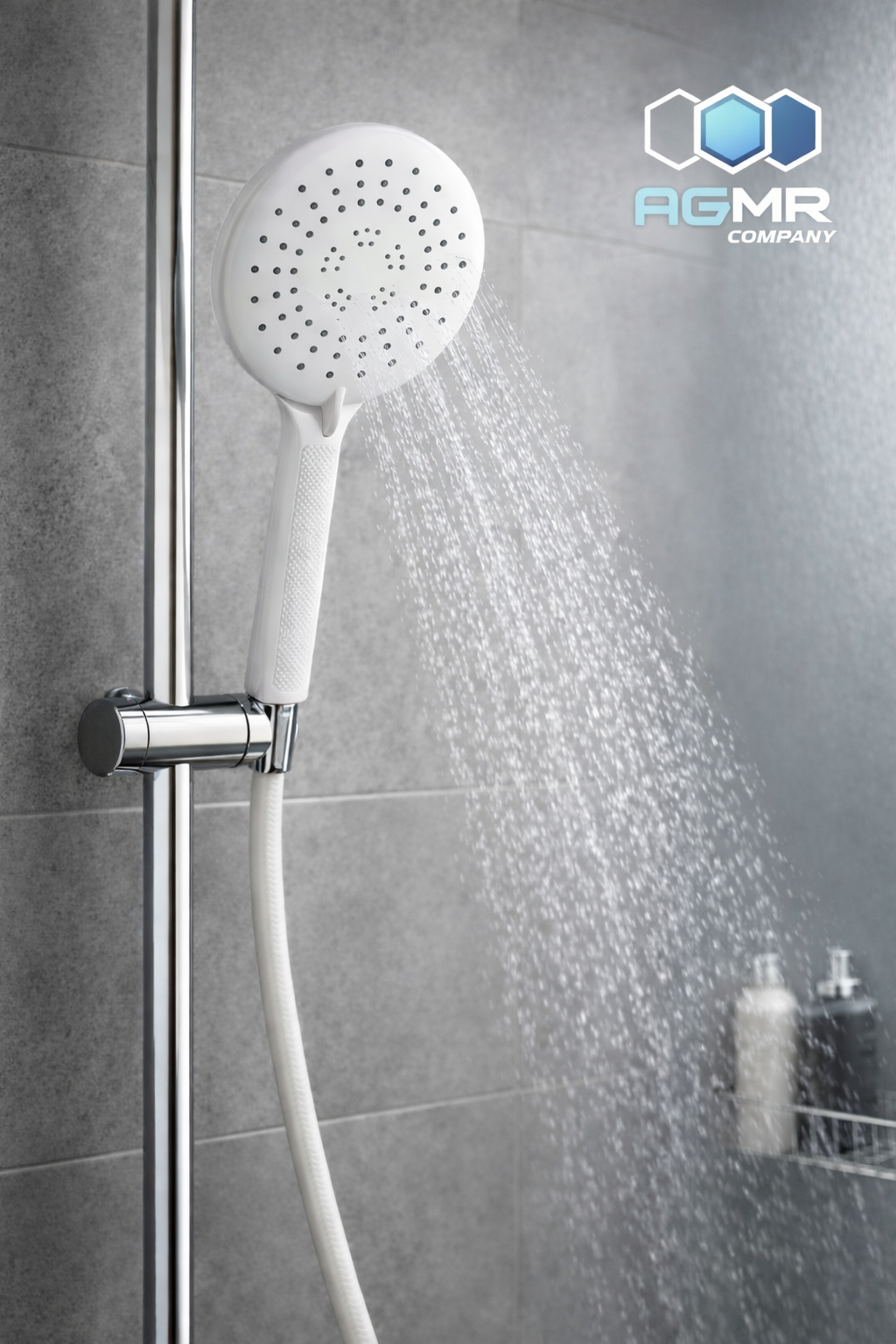 A white showerhead attached to a metal rail with water flowing from it in a modern bathroom with gray tiled walls and bottles on a built-in shelf.