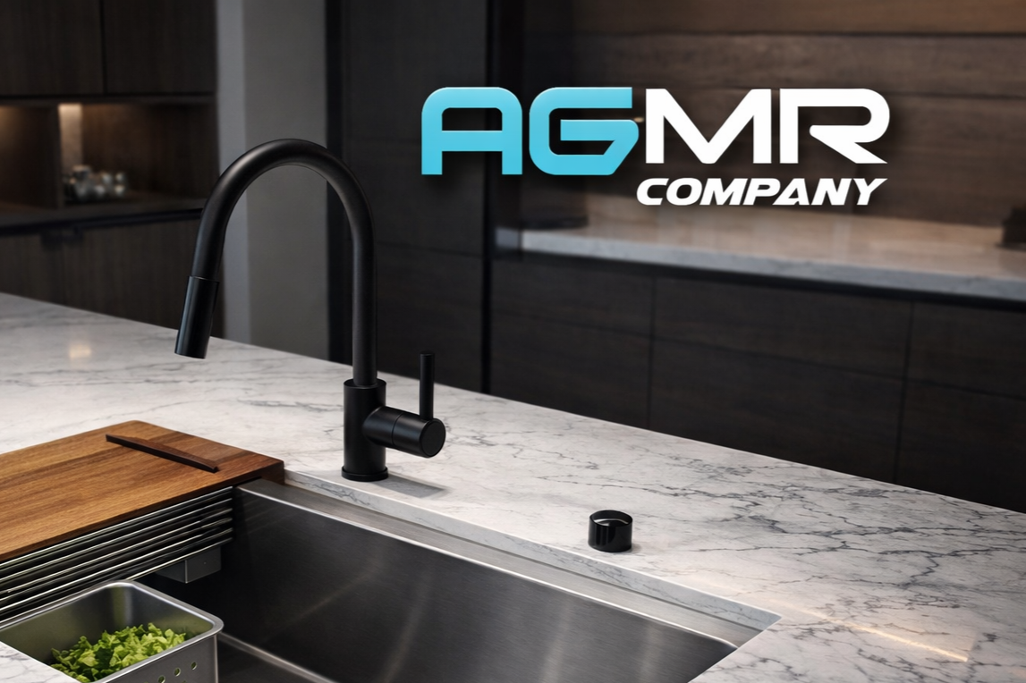 Modern kitchen sink with black faucet, wooden cutting board, and a container of lettuce on a white marble countertop in a kitchen with dark wood cabinets and a logo that reads 'AGMR Company' in the background.