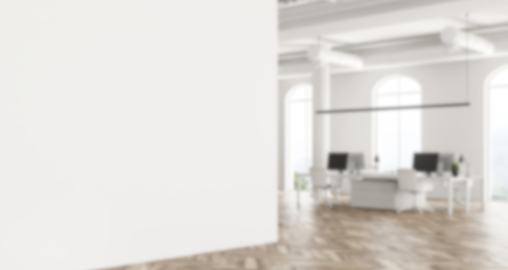 Espaço de escritório com paredes brancas, janelas grandes com moldura ar moderna, piso de madeira, mesas brancas com computadores e cadeiras brancas, luminárias penduradas e plantas decorativas.