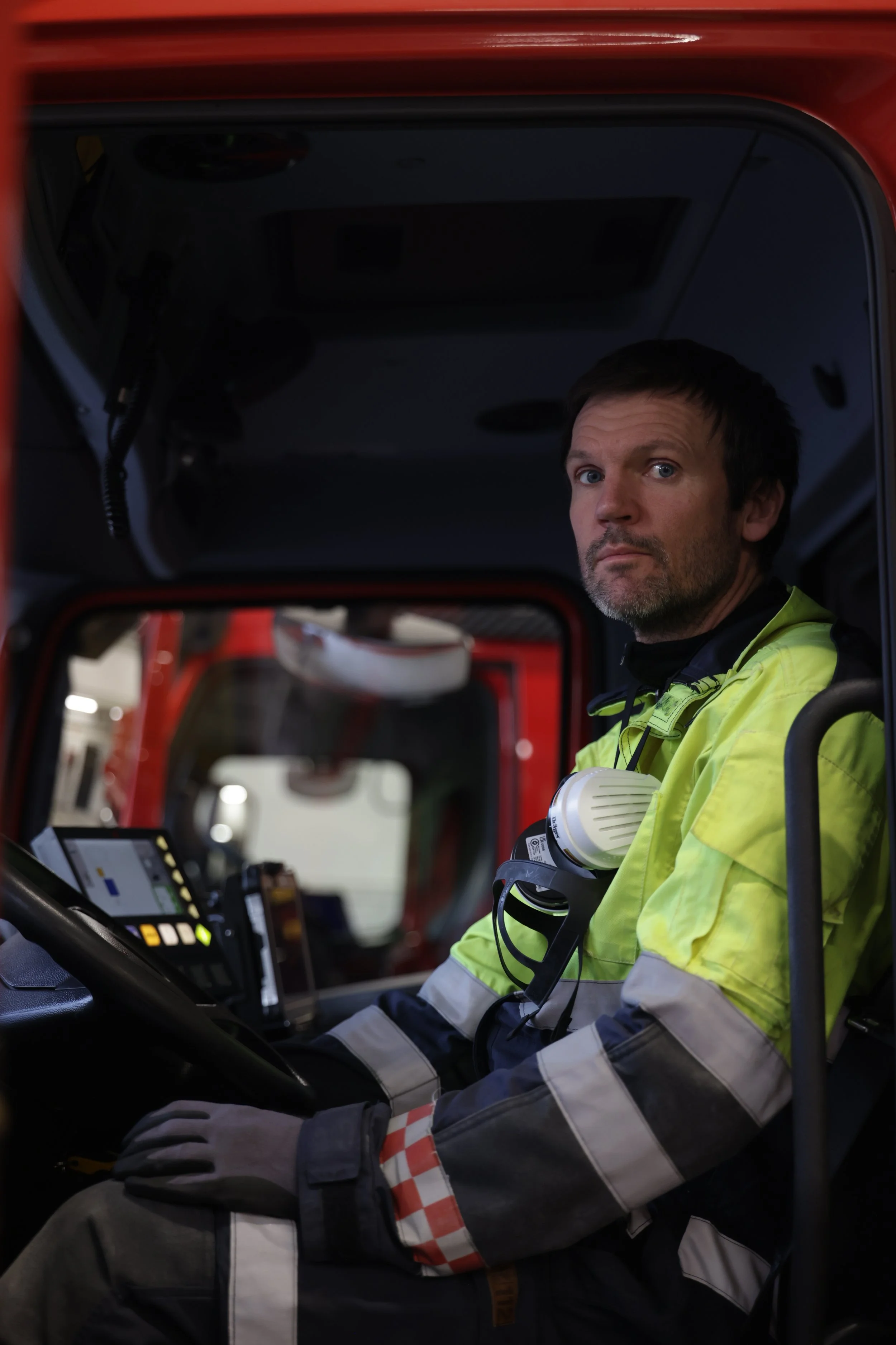 En mann i et høyt synlig arbeidsantrekk, sittende i førersetet på en redningsbil.