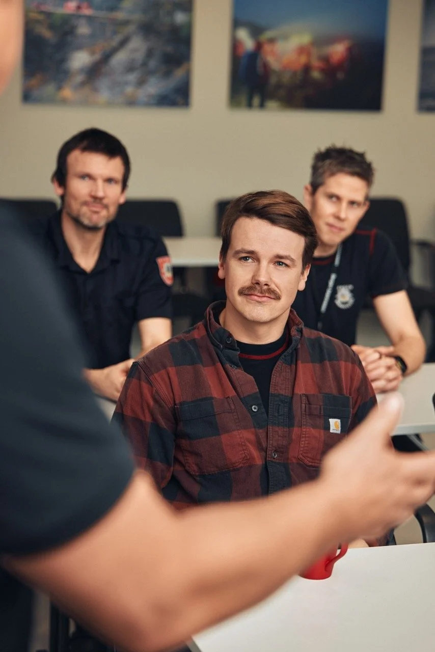 Tre menn sitter i et møterom, en av dem snakker mens de andre lytter.