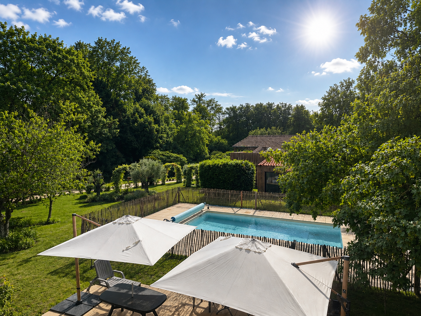 Piscine extérieure avec jouets gonflables, parasol coloré et chaises longues, entourée d'une clôture en bois et de plantes, sous un ciel bleu.