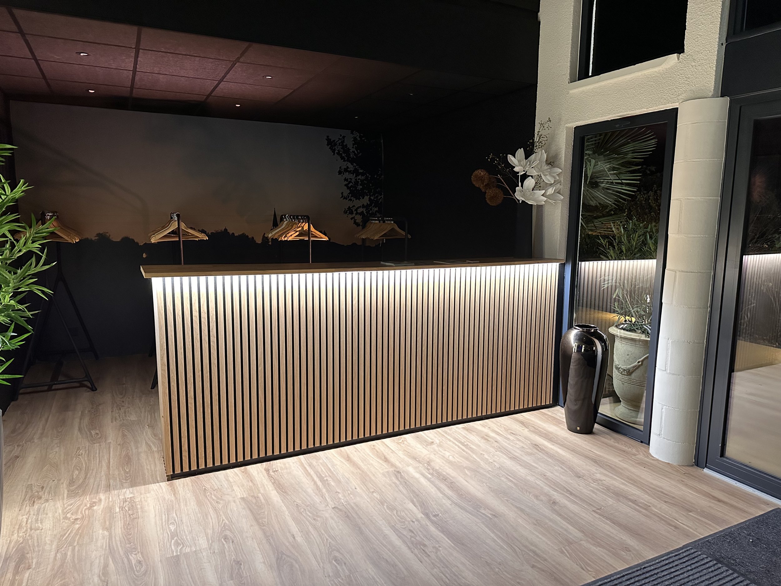 Intérieur moderne avec un comptoir en bois éclairé, plantes et une grande fenêtre avec un décor élégant.