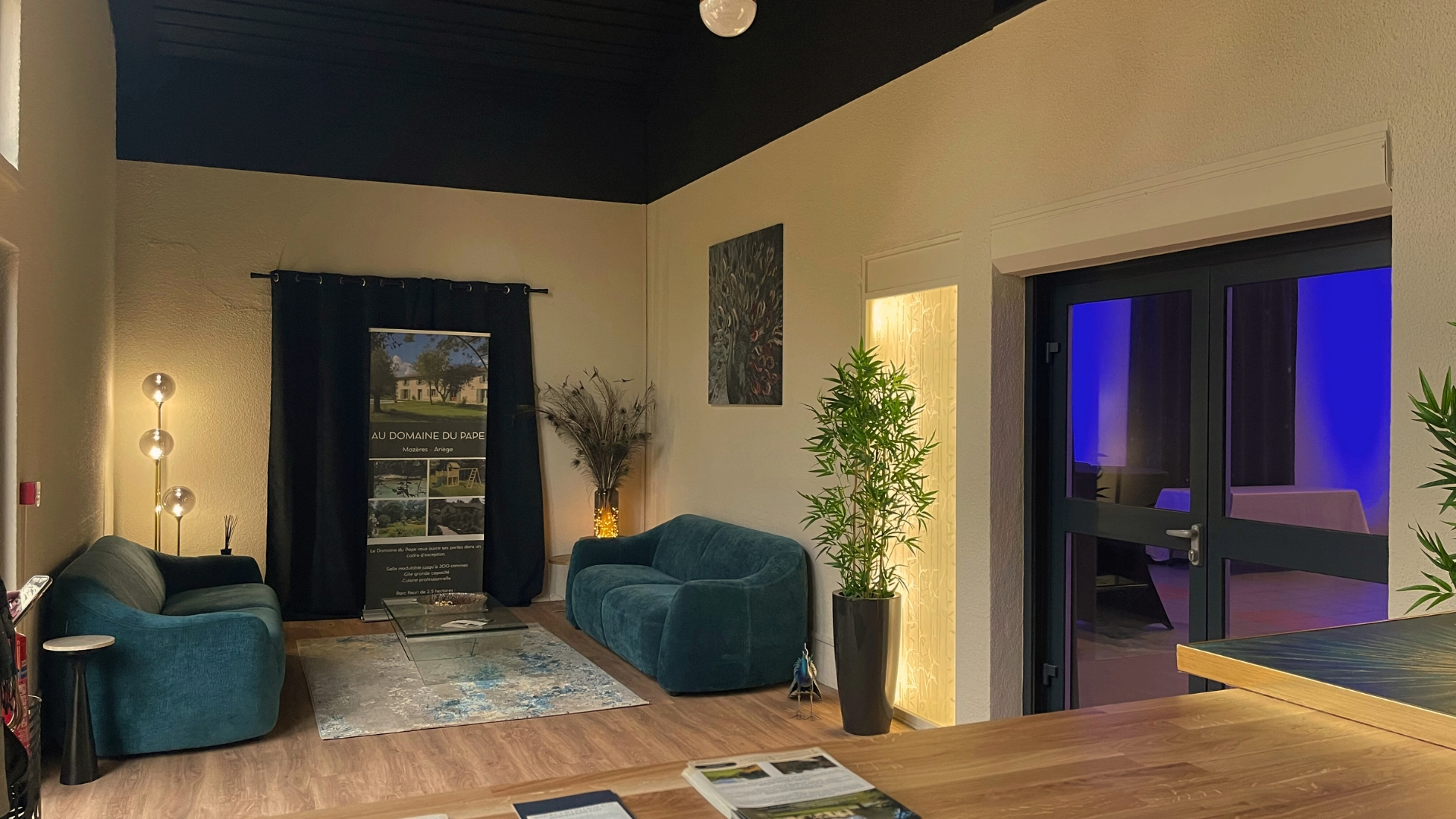 Un salon modernes avec deux canapés bleus, une grande plante verte, un tapis, des lampes et une baie vitrée avec ambiance bleue