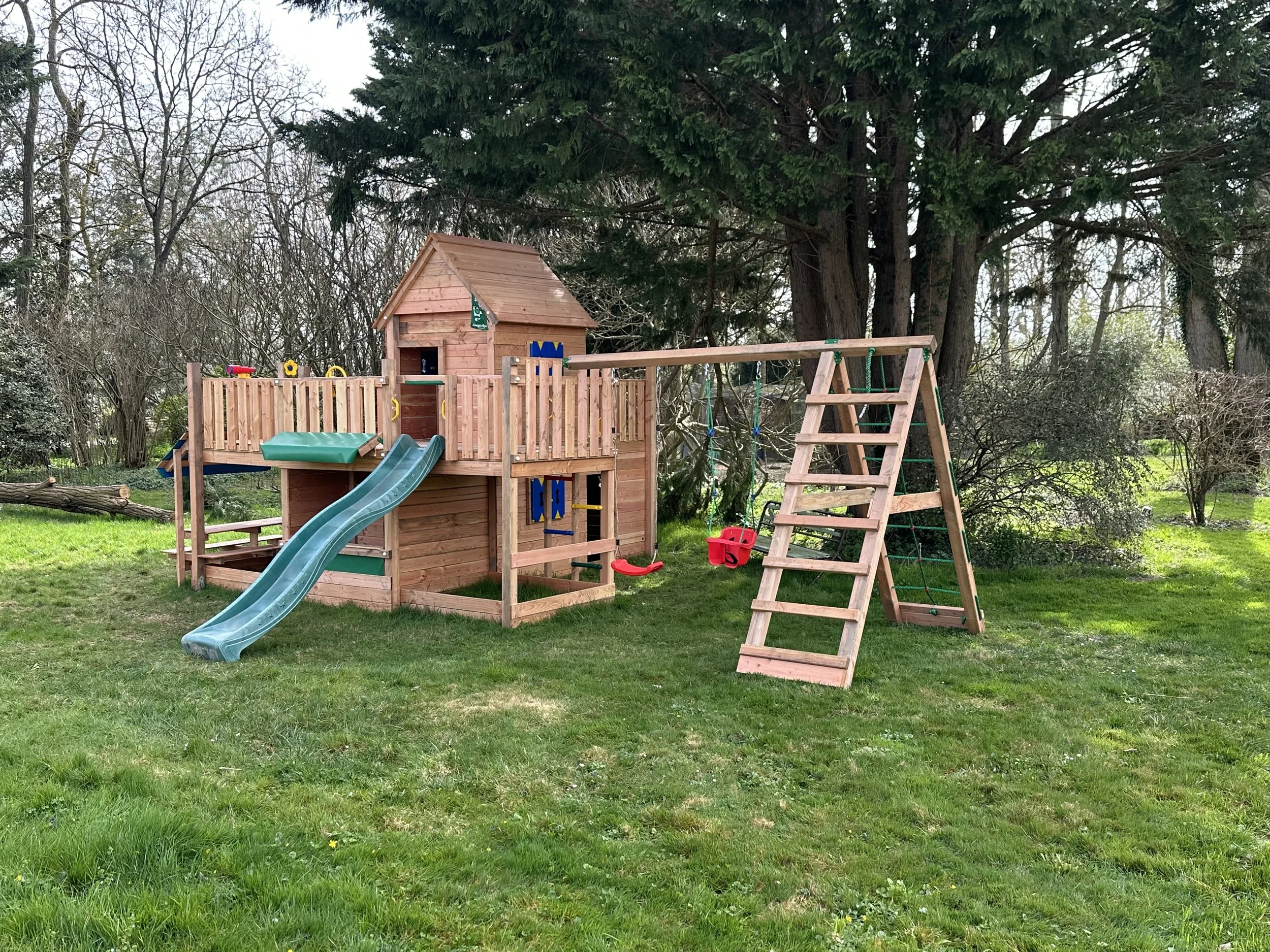 Une aire de jeux pour enfants avec deux balançoires, un toboggan et une cabane