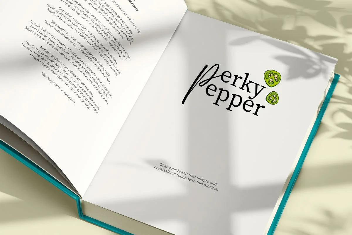 Open book displaying a logo that reads 'Perky Pepper' with stylized green peppers, on a light surface with shadows from nearby foliage.