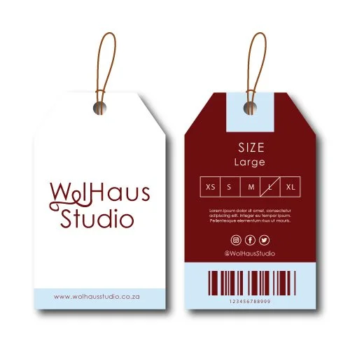 Two clothing tags, one white and one maroon, with strings attached. The white tag displays the logo 'WolHaus Studio' and website, while the maroon tag shows size information and a barcode.