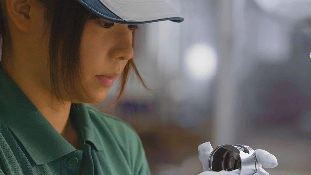 Delavka v proizvodnem okolju natančno pregleduje kovinski sestavni del ECHO orodja, kar poudarja kakovost, natančno izdelavo in nadzor proizvodnje.