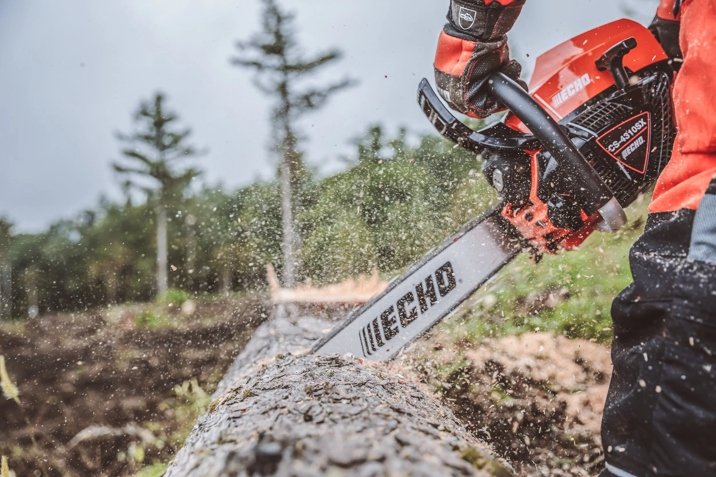 Motorna žaga ECHO CS-4310S v uporabi pri rezanju hloda na prostem, z vidnimi lesnimi ostružki, ki letijo med rezanjem.