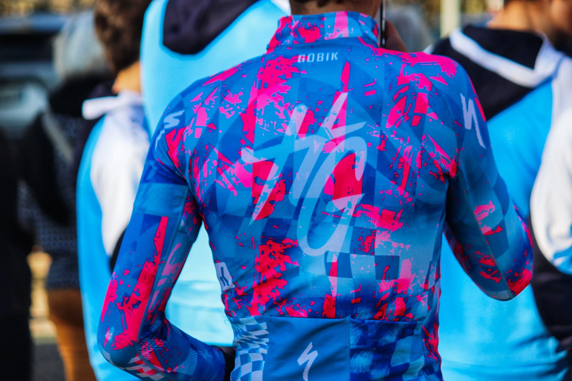 Personne portant une veste d'extérieur bleu et rose flashy, visible de dos, dans une foule.