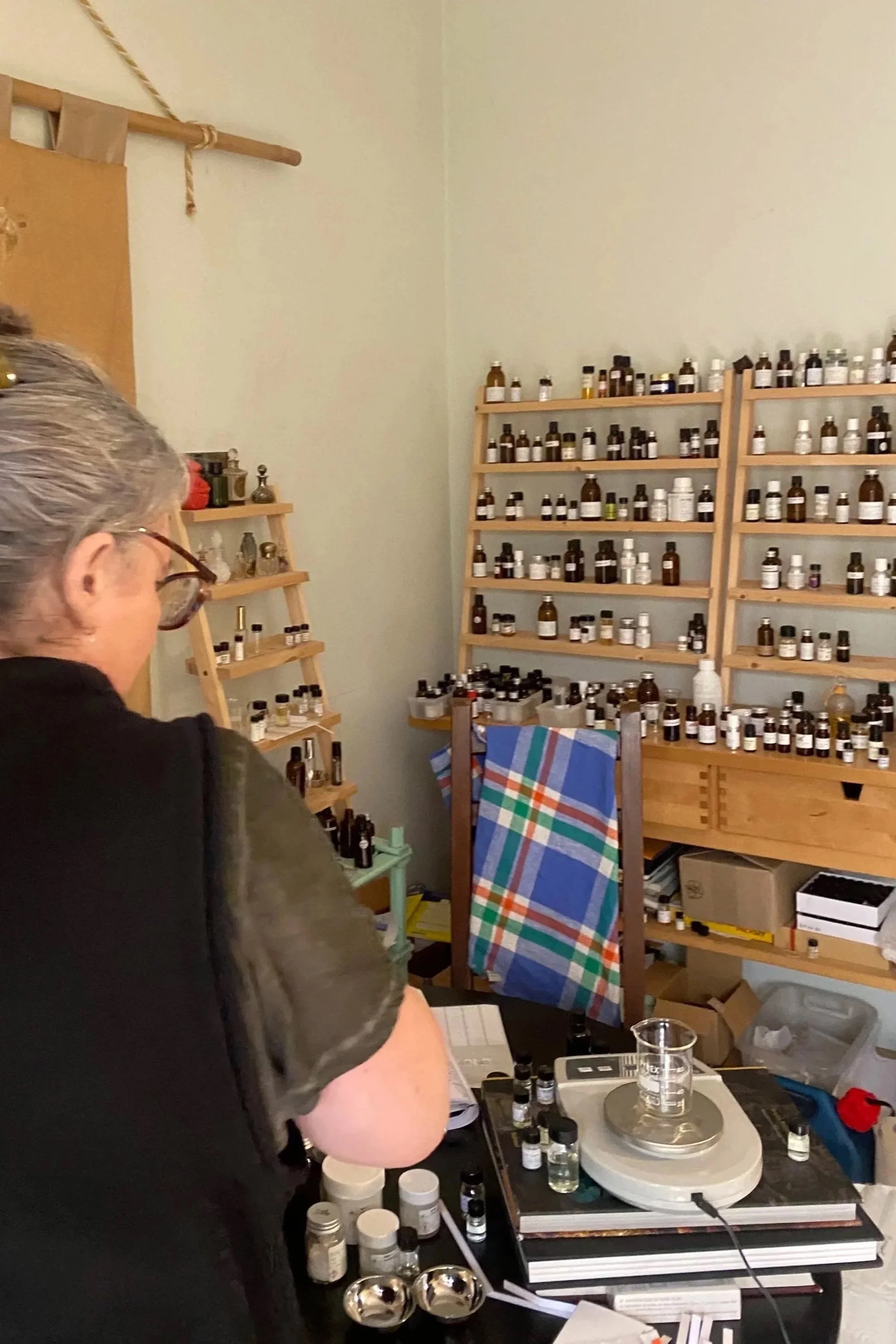 Une femme dans un laboratoire avec des étagères remplies de petites bouteilles en verre contenant diverses substances, utilisant du matériel de laboratoire sur un comptoir.