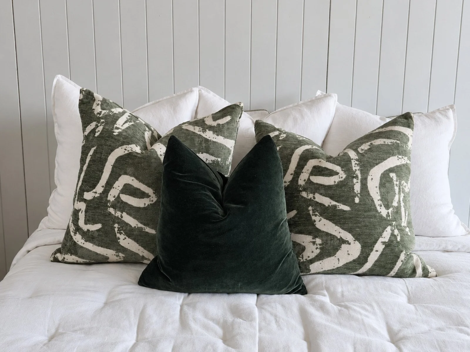 Custom made olive green patterned and velvet cushions on a white bed