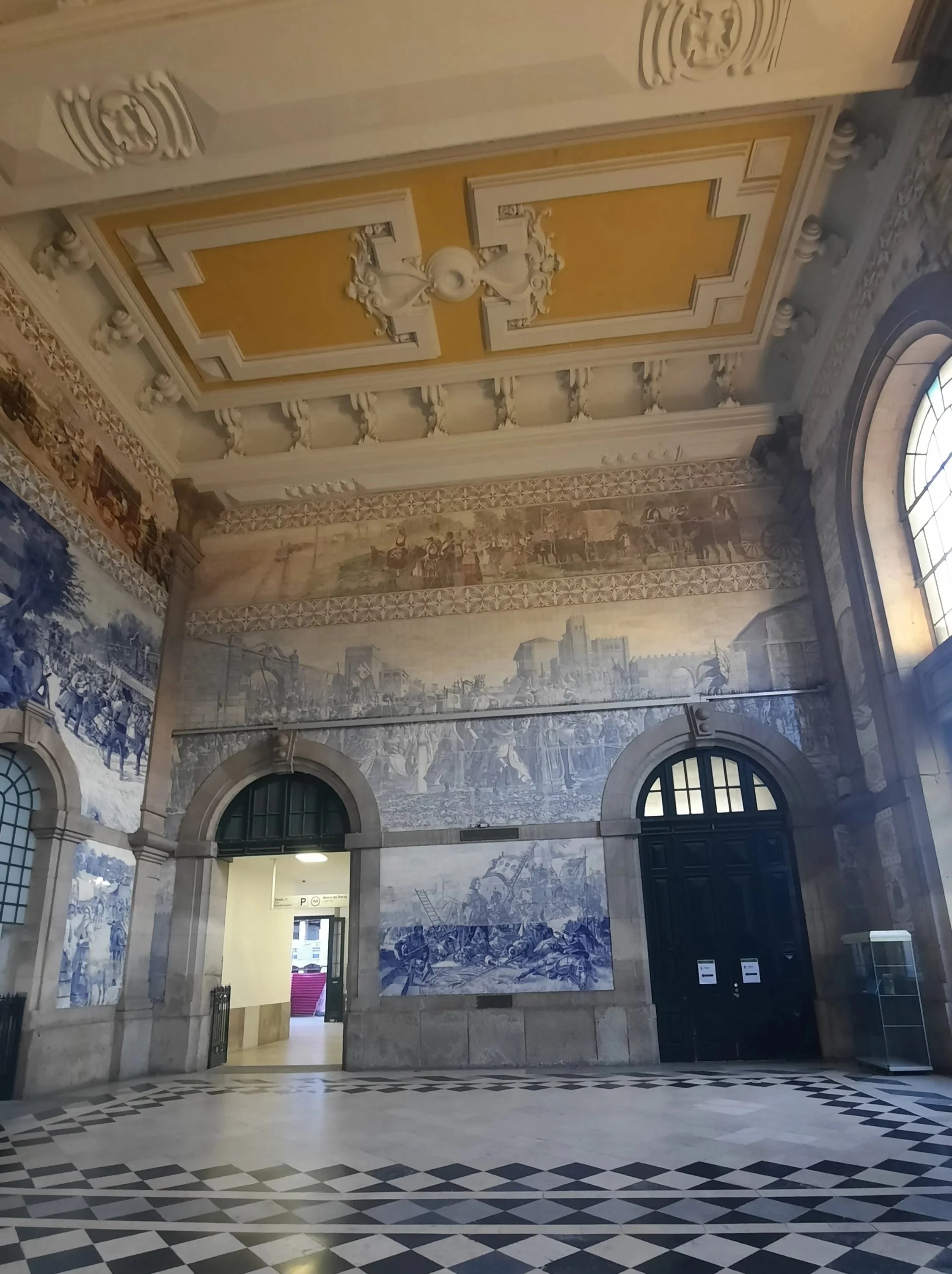 Intérieur d'un bâtiment historique avec murs décorés de fresques en bleu et blanc, hauts plafonds avec moulures et unités d'information à gauche et à droite.