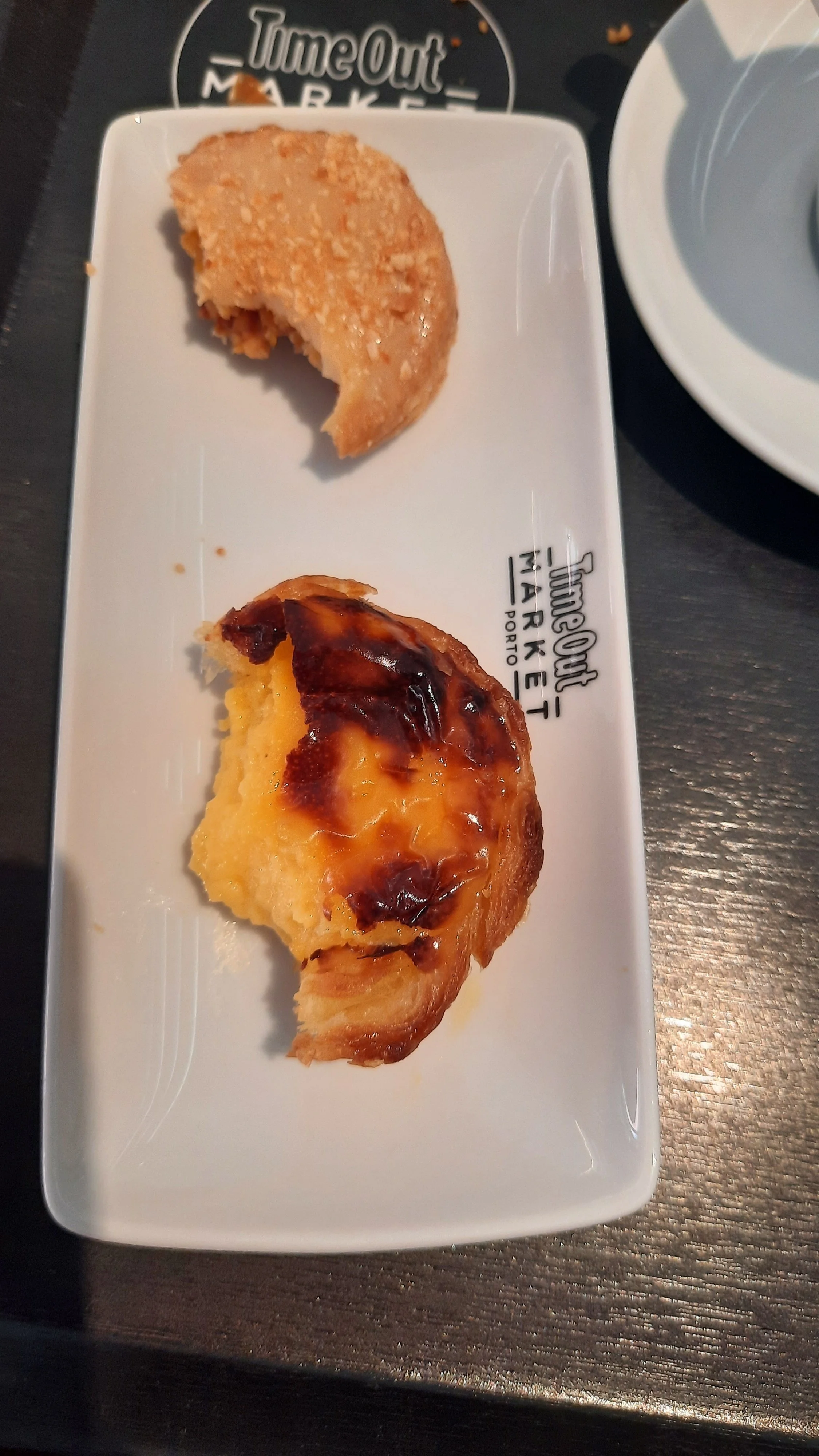 Deux morceaux de tarte, une tarte aux pommes avec une garniture caramélisée, sur une assiette blanche placée sur une table sombre.