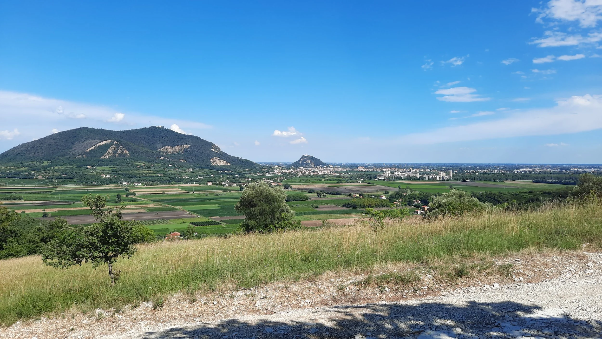Vue panoramique de champs agricoles avec des collines et une ville en arrière-plan sous un ciel bleu avec quelques nuages.