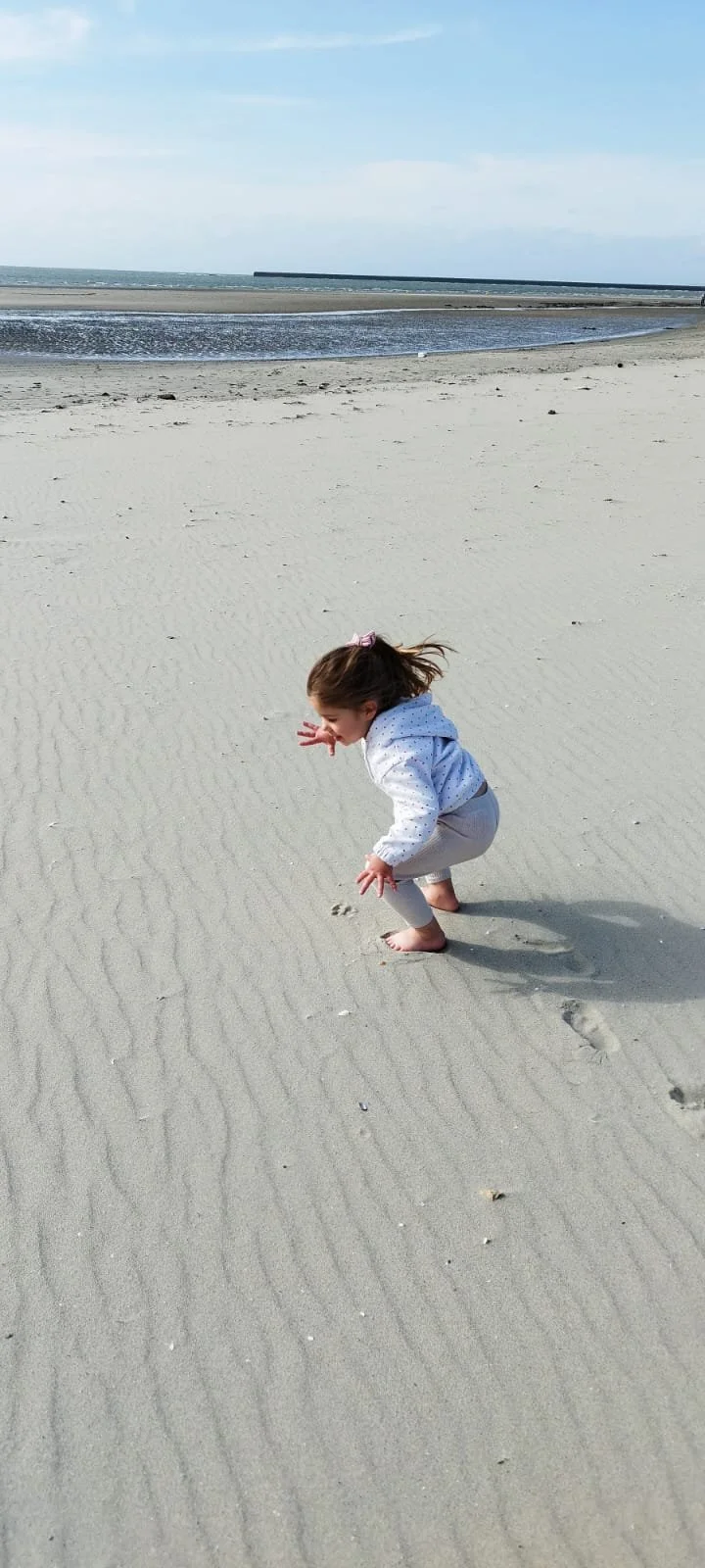 Jeune fille jouant dans le sable sur la plage, avec la mer et un ciel bleu en arrière-plan.