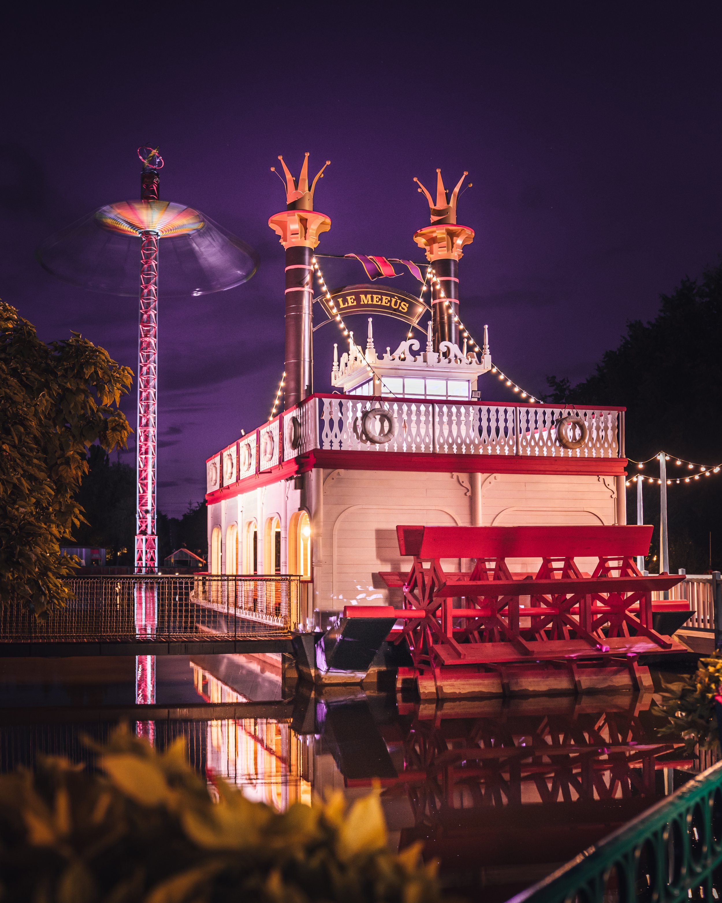 Nuit à la fête foraine avec une maison hantée en lumière, un siège de chute libre en mouvement, et des décorations lumineuses