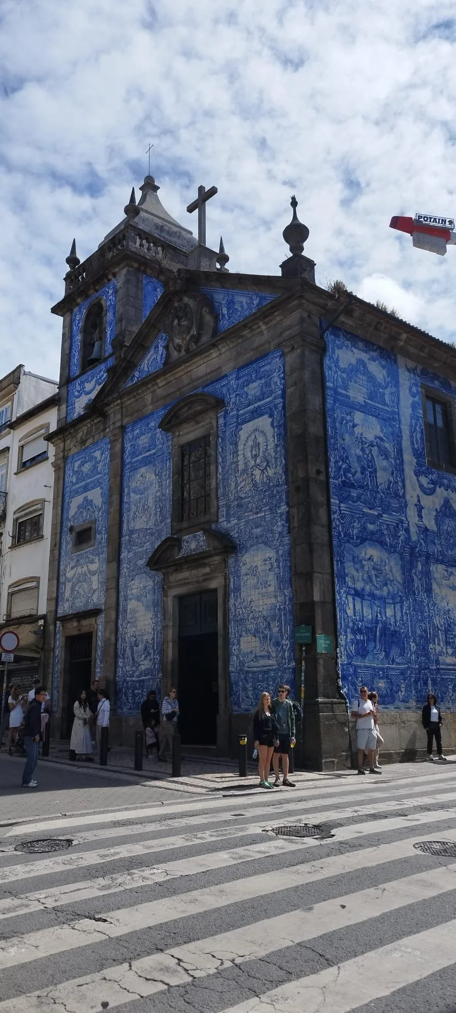 Une église ornée de carreaux de faïence bleue avec des motifs complexes, située dans une zone urbaine piétonne, avec plusieurs personnes qui attendent ou se croisent devant l'entrée.