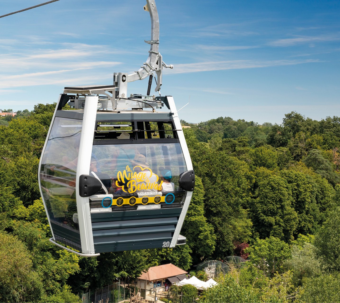 Une cabine de téléphérique suspendue dans les airs au-dessus d'une forêt dense avec des arbres verts et un ciel bleu clair.
