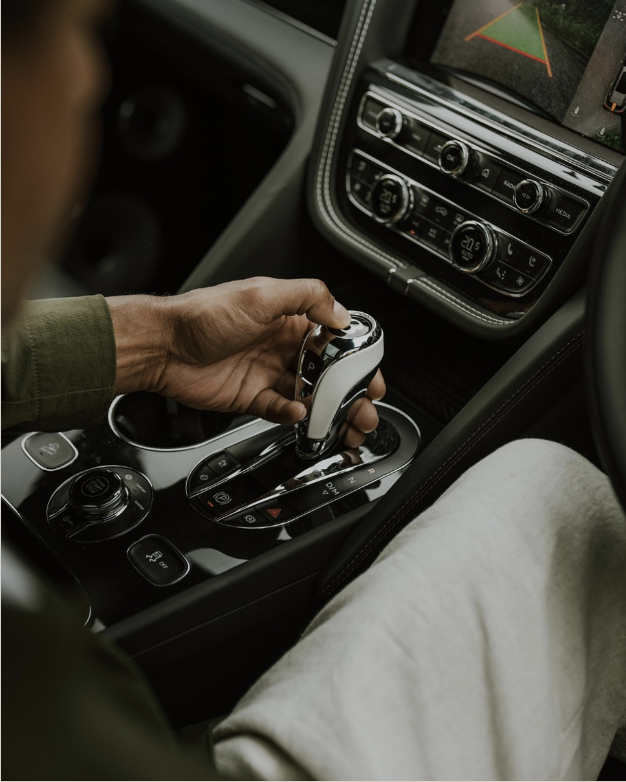 A person operating a modern automatic transmission car gear shift inside a vehicle, with the dashboard and infotainment system visible.