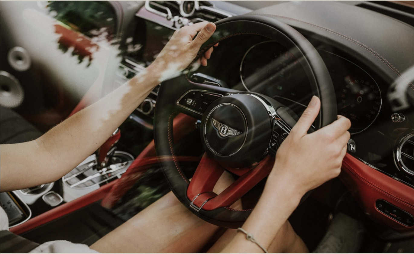 Interior view of a person driving a luxury Bentley car, focusing on hands gripping the steering wheel.