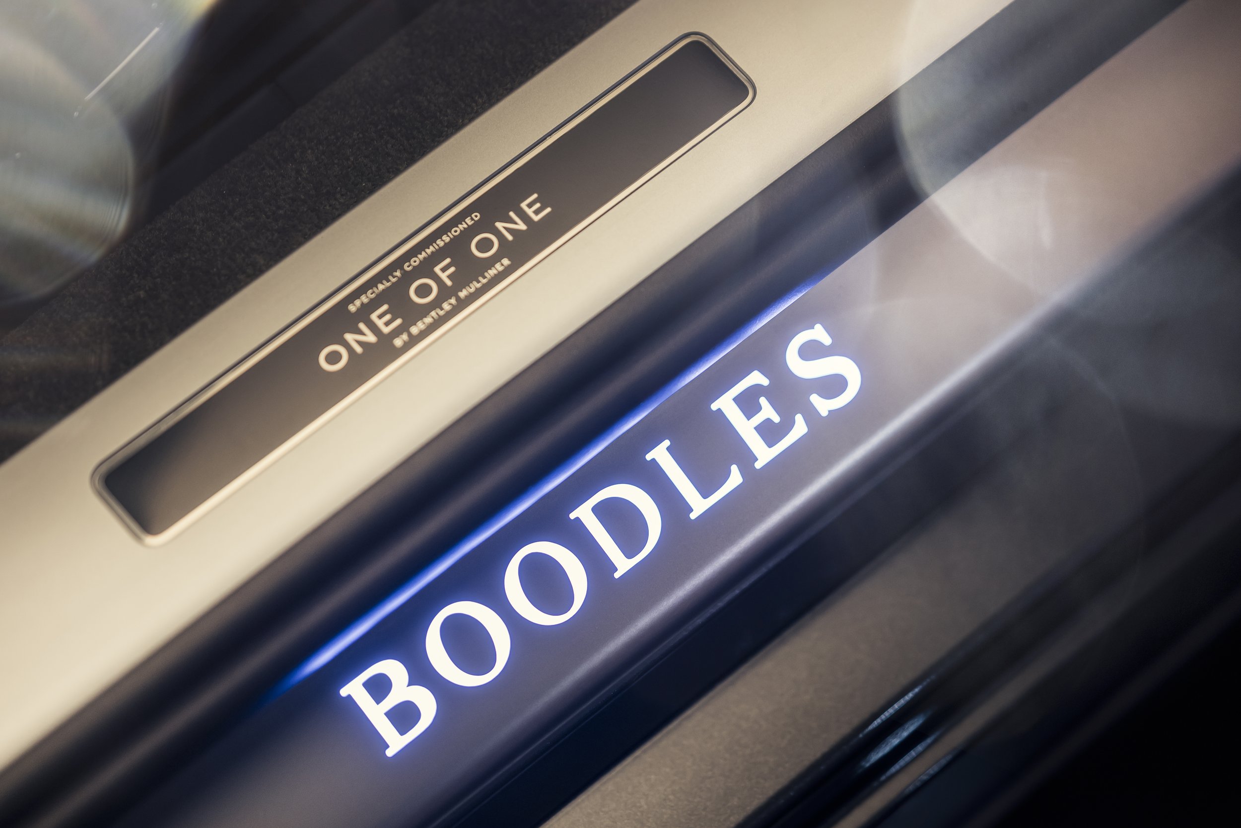 Close-up of an elevator floor indicator with the words 'BOOKIES' illuminated in white and an adjacent panel labeled 'ONE OF ONE' with smaller text indicating it is specially commissioned by Bettye Mullins.