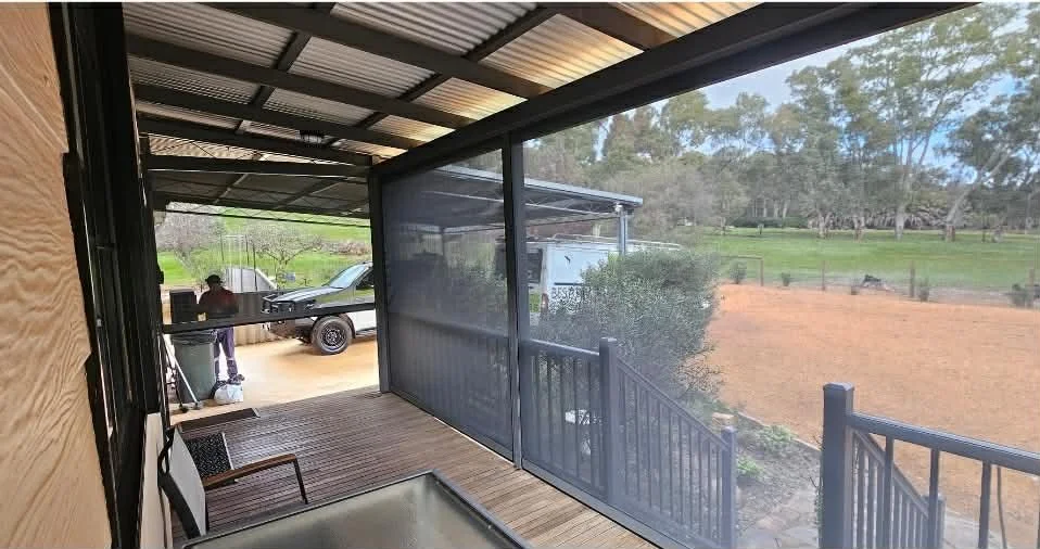 View from a screened porch or balcony overlooking a rural property with a parked truck and a person working outside, with trees and open land in the background.