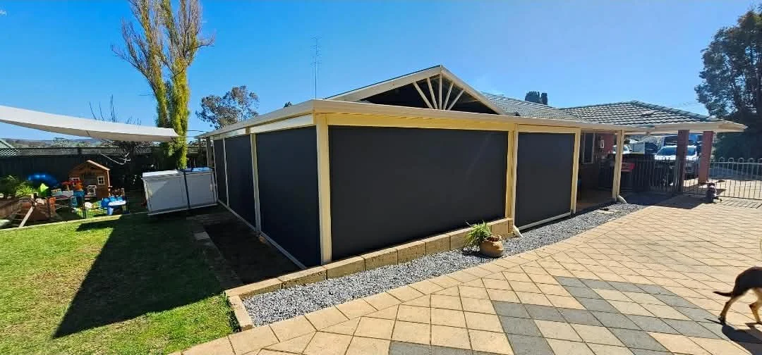 Backyard with a black screened enclosure, a small grassy area, potted plant, paved patio, and a dog in the lower right corner.