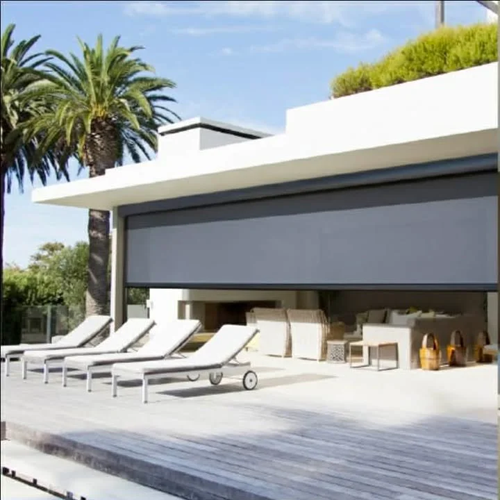 Modern house with a retractable gray shade, outdoor lounge chairs, and patio furniture, surrounded by palm trees and green shrubs.