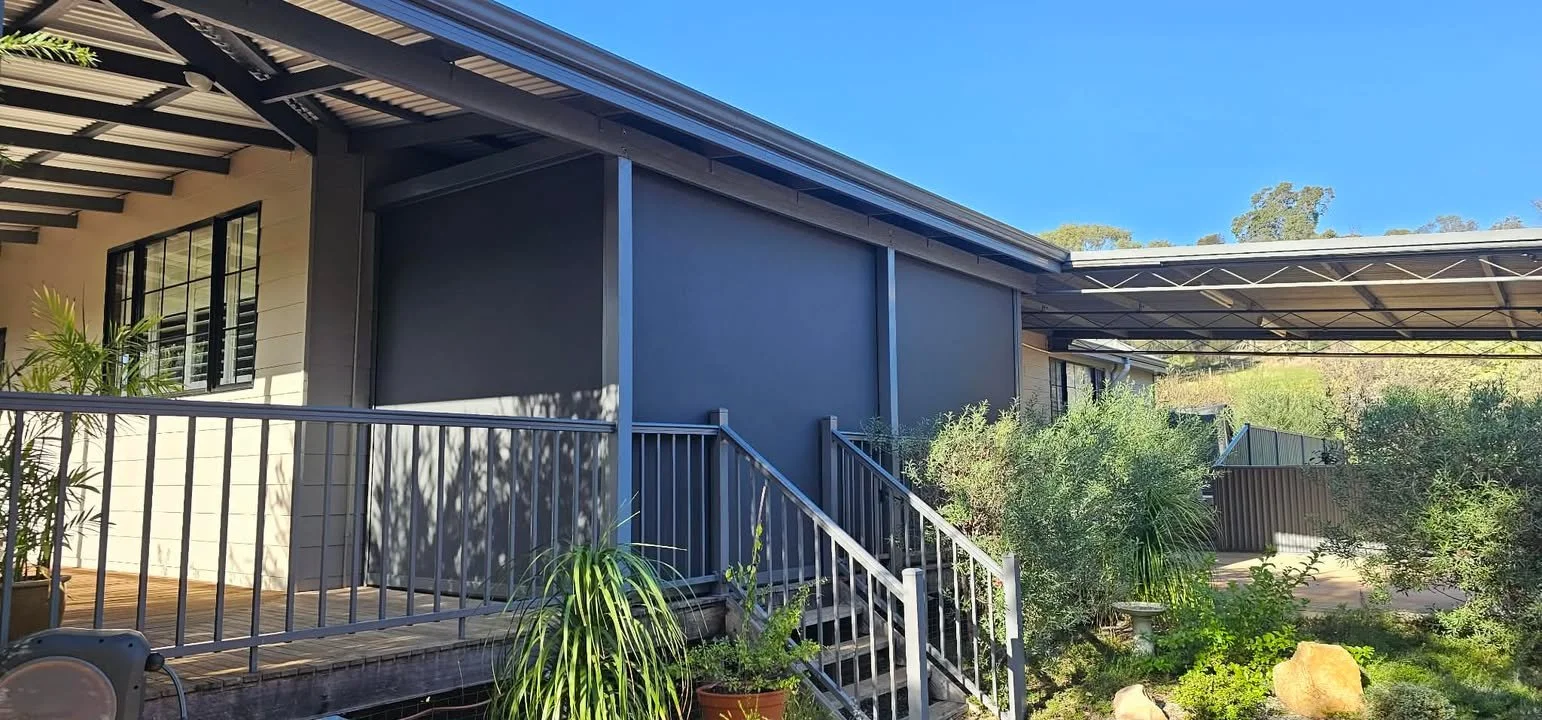 A modern house with a screened-in porch, stairs leading up to the porch, surrounding greenery, potted plants, and a blue sky.