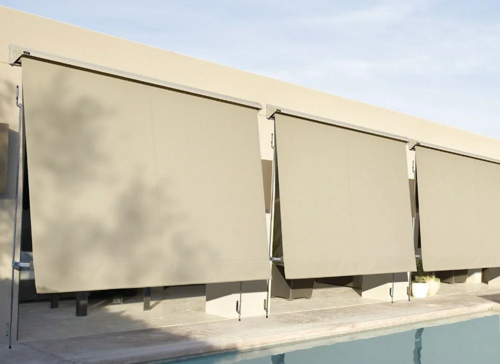 A modern building with three large beige retractable shades or awnings, adjacent to a swimming pool.