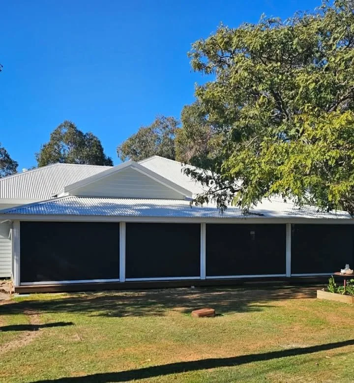 Backyard with screened porch, green grass, a tree on the right, and a house with a white metal roof in the background, under a blue sky.