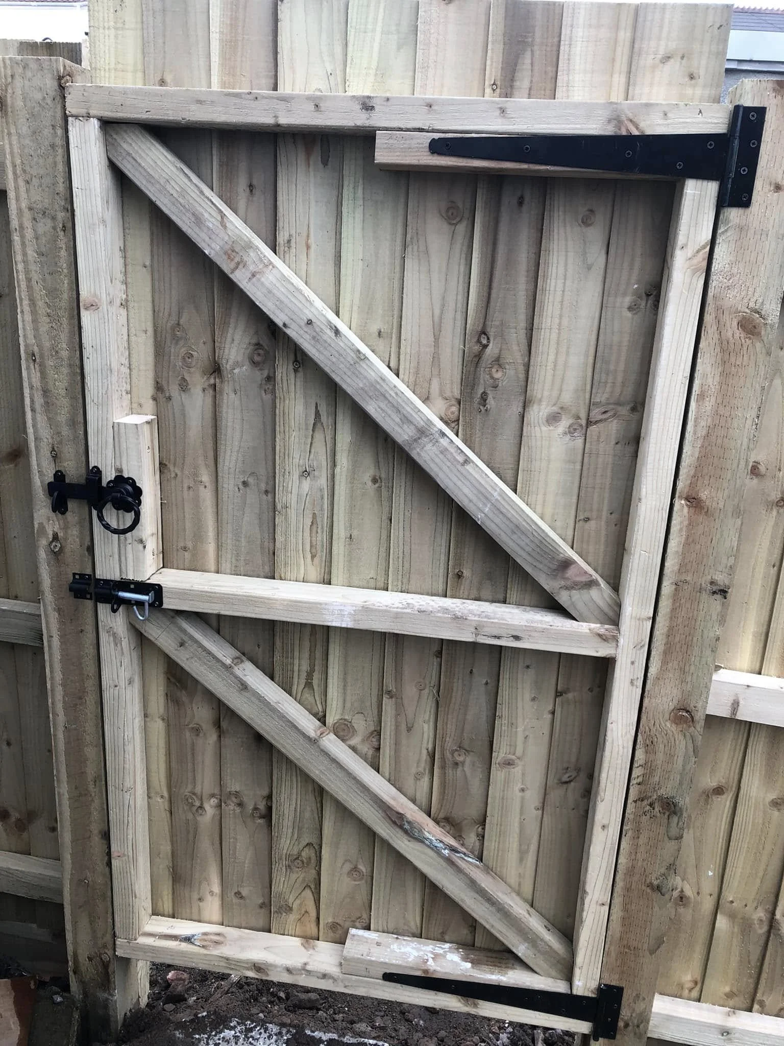 A new wooden gate with diagonal and horizontal support beams, installed on a fence with metal hinges and latch.