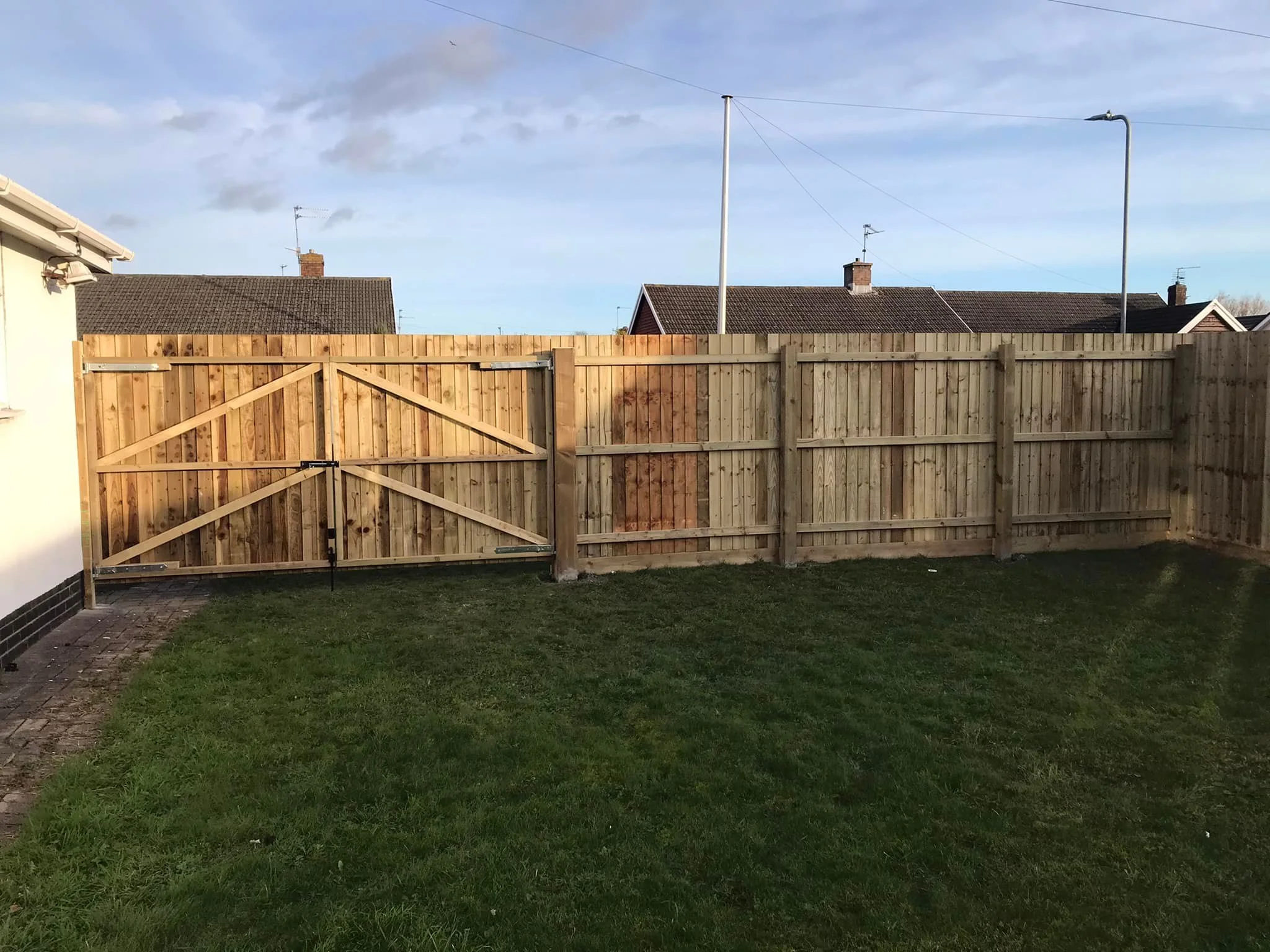 A backyard with a wooden fence, a gate, and a grassy lawn.