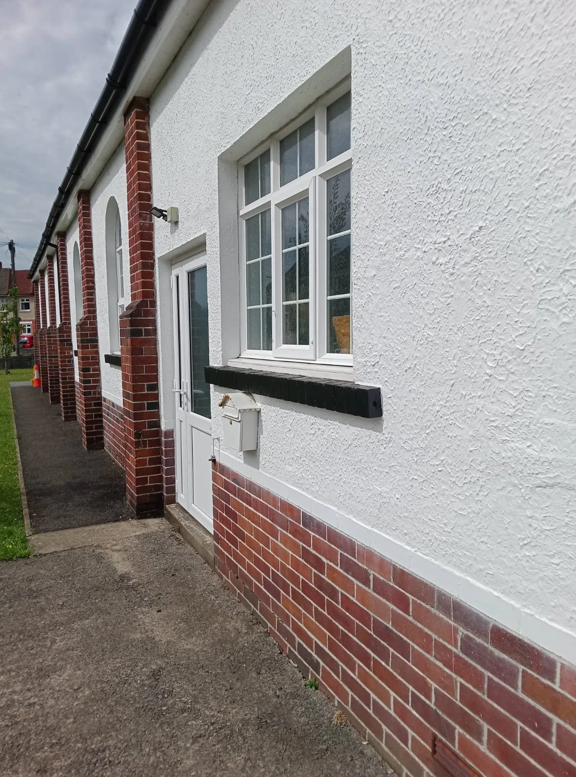 A freshly painted house with white textured walls and red brick lower sections.