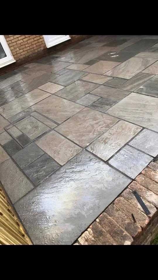 Wet stone patio with rectangular gray and beige paving stones next to a brick wall and sliding glass door.