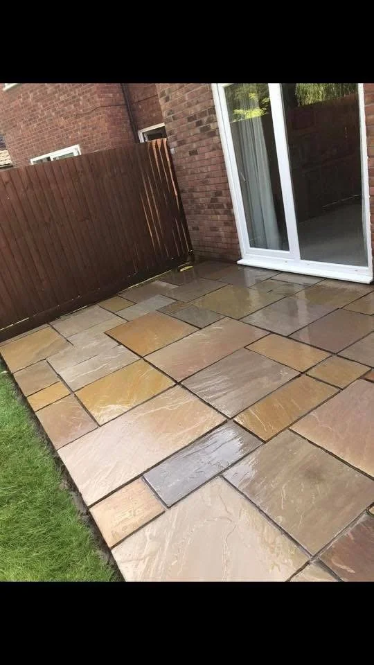 Wet stone patio next to a brick house with a sliding glass door and a wooden fence.