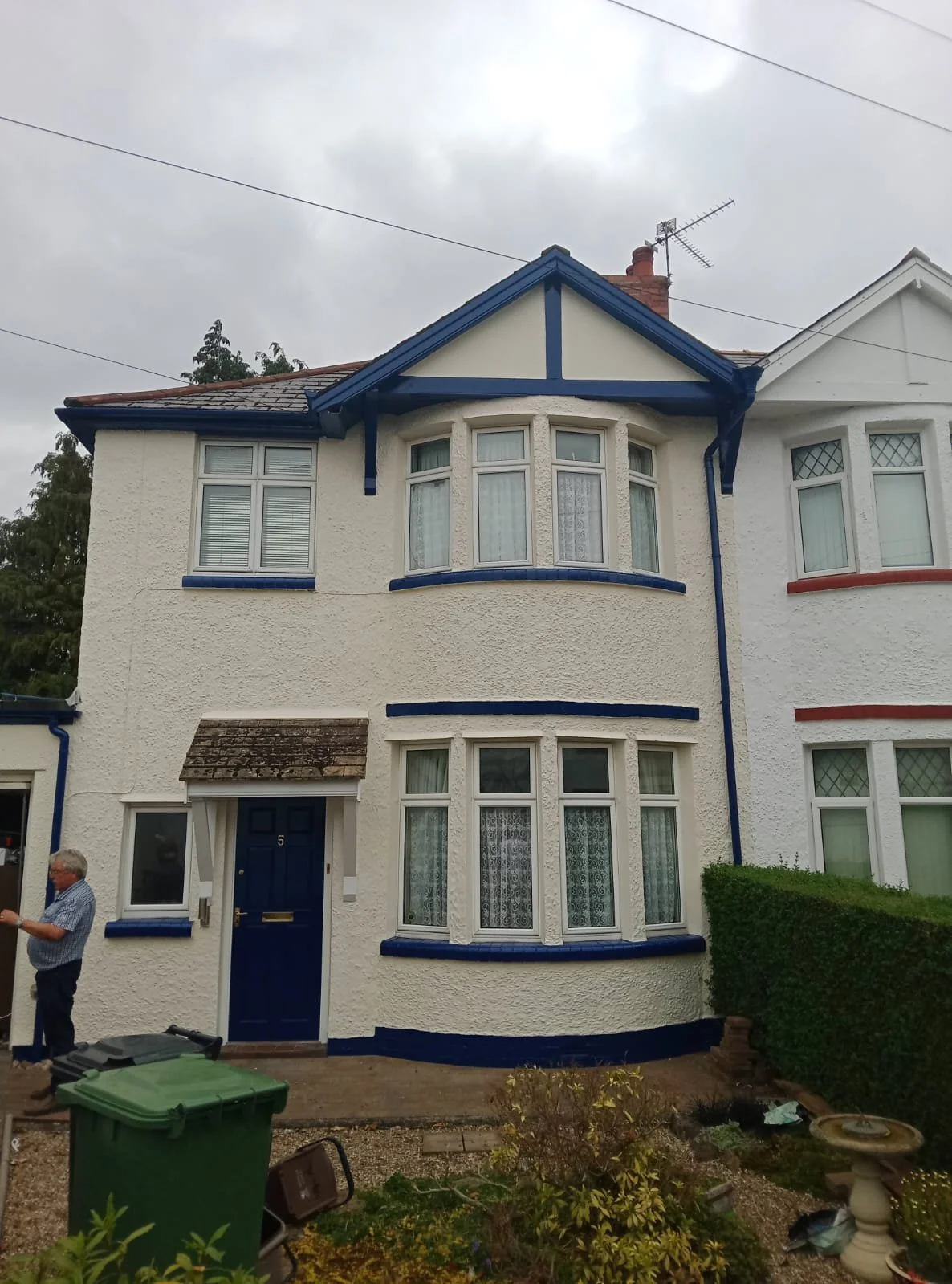 A two-story white house with blue trim and a bay window, with a dark blue front door and a small porch roof. Freshly painted exterior.