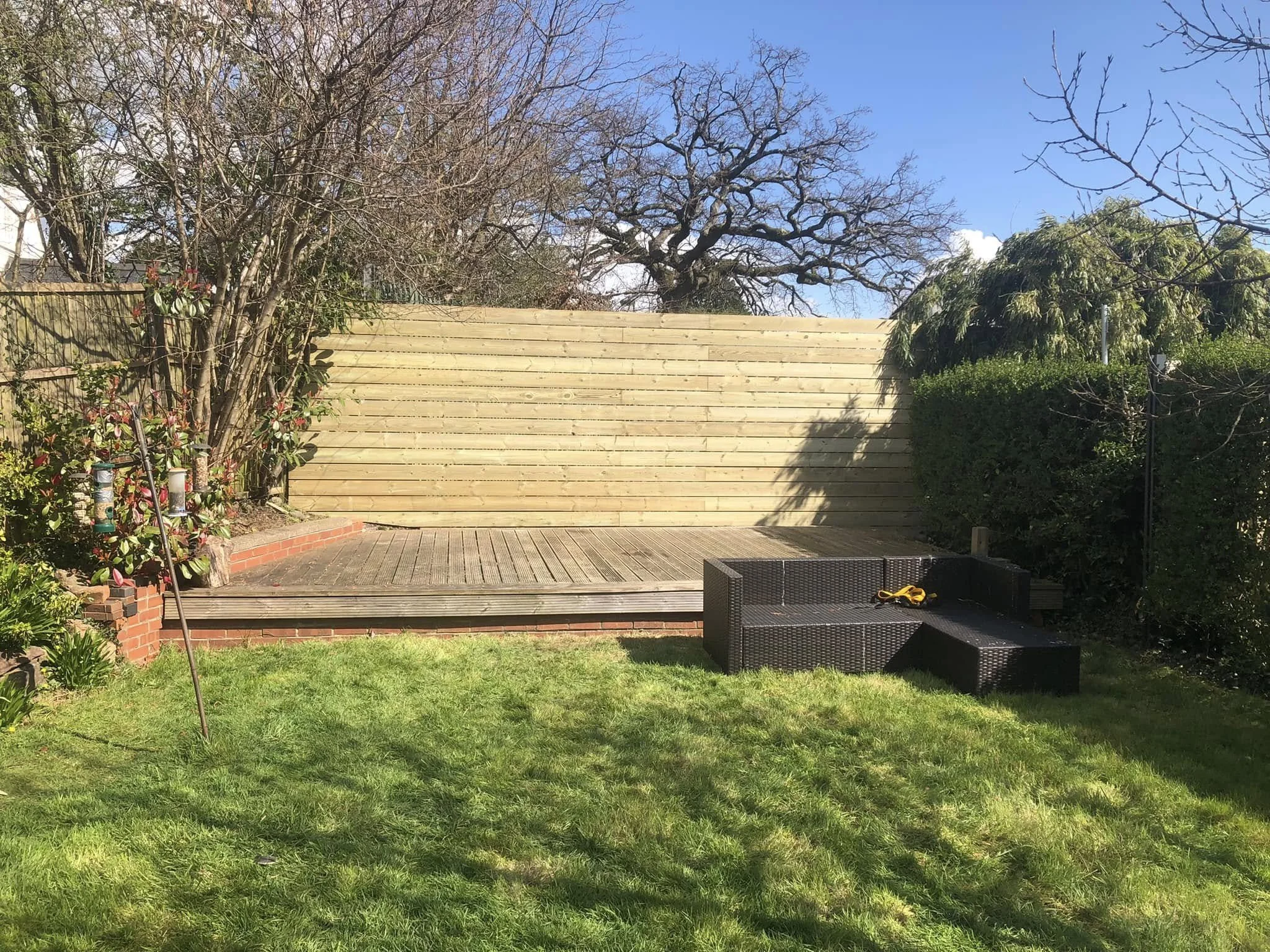A backyard with a grassy lawn, a wooden deck, and a garden fence. 
