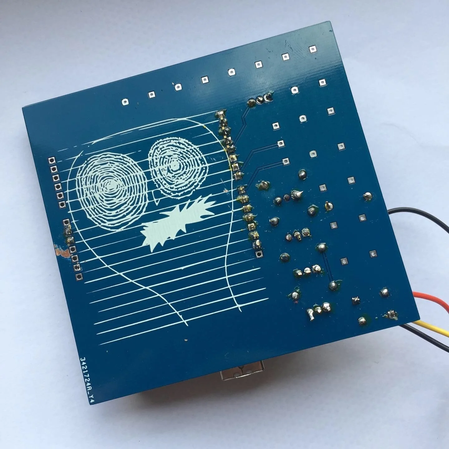 A blue printed circuit board with fingerprint patterns and a stylized face design, connected to wires, and electronic components with soldered connections.
