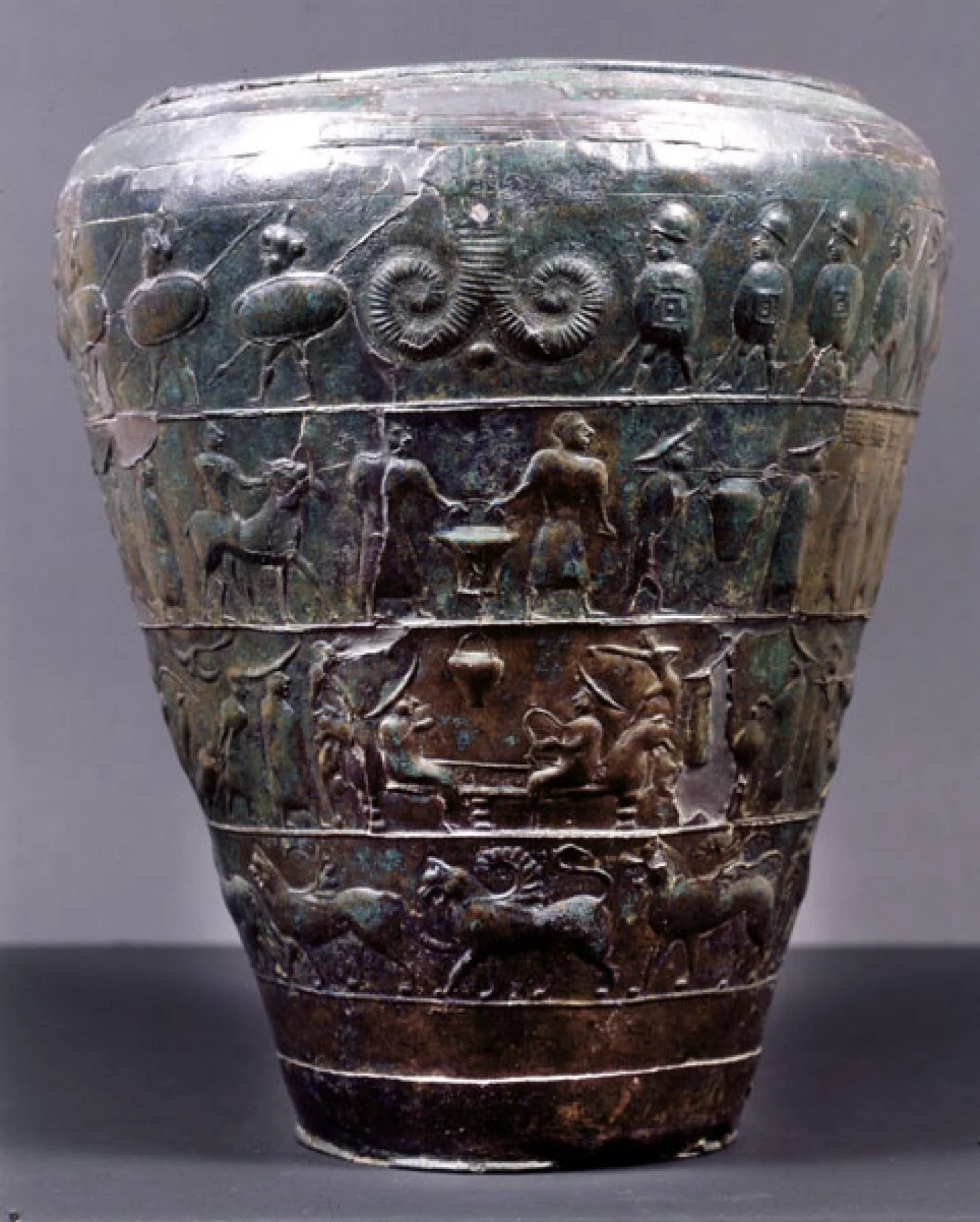 Ancient decorated bronze vase with detailed relief carvings of animals, humans, and abstract patterns.