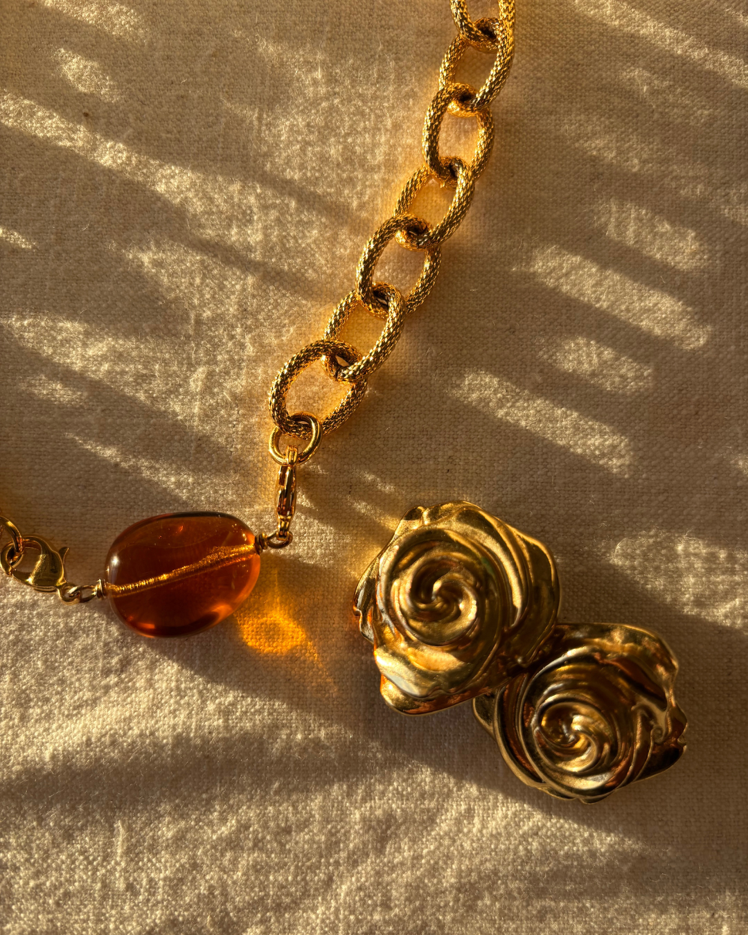 Une chaîne en or avec des pendentifs en forme de spirales et une pierre orange translucide, éclairée par une lumière chaude sur un tissu satiné.