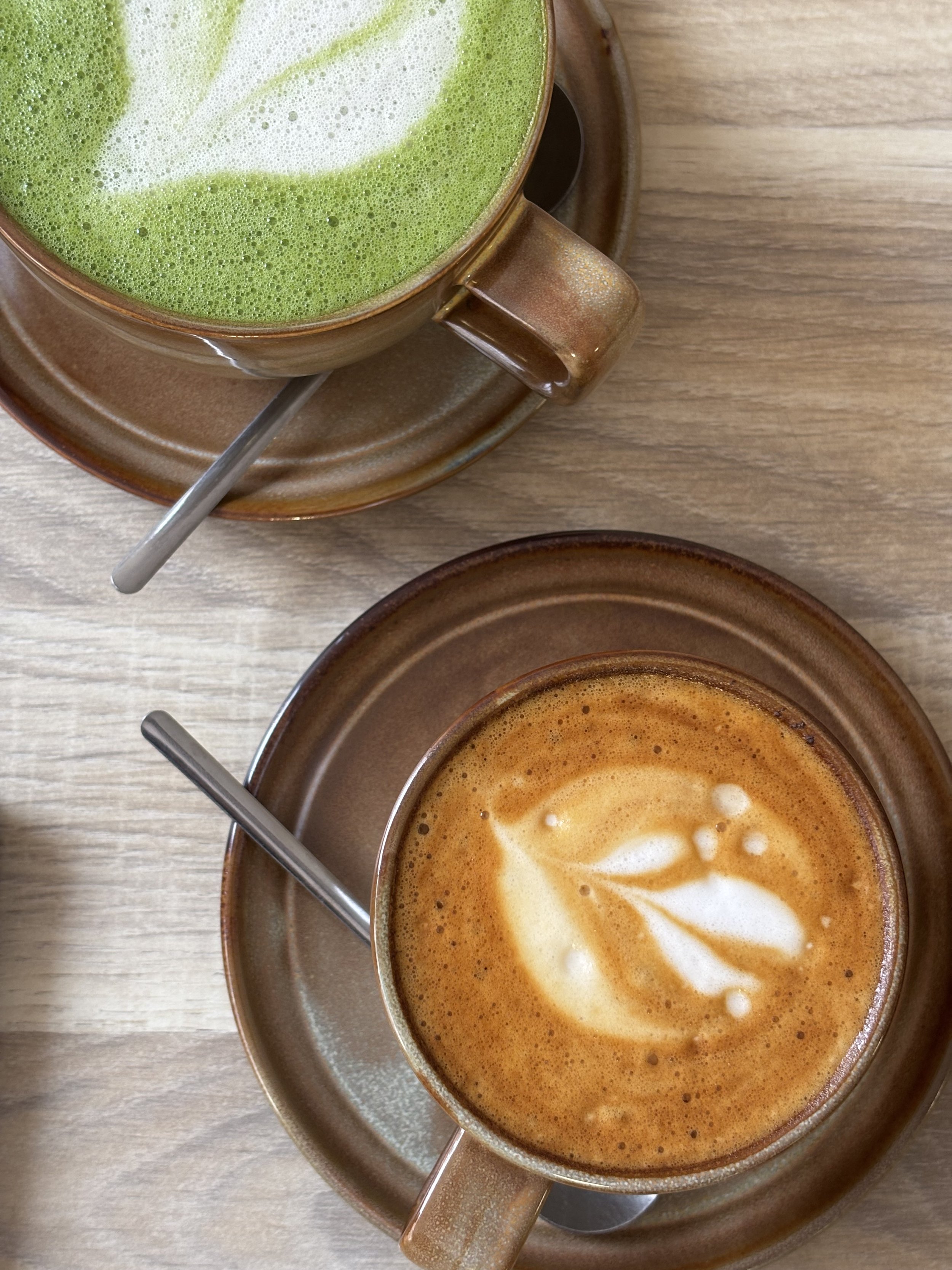 Deux tasses de café avec milkfoam et une mousse des feuilles de matcha vert dans une tasse, sur une table en bois.