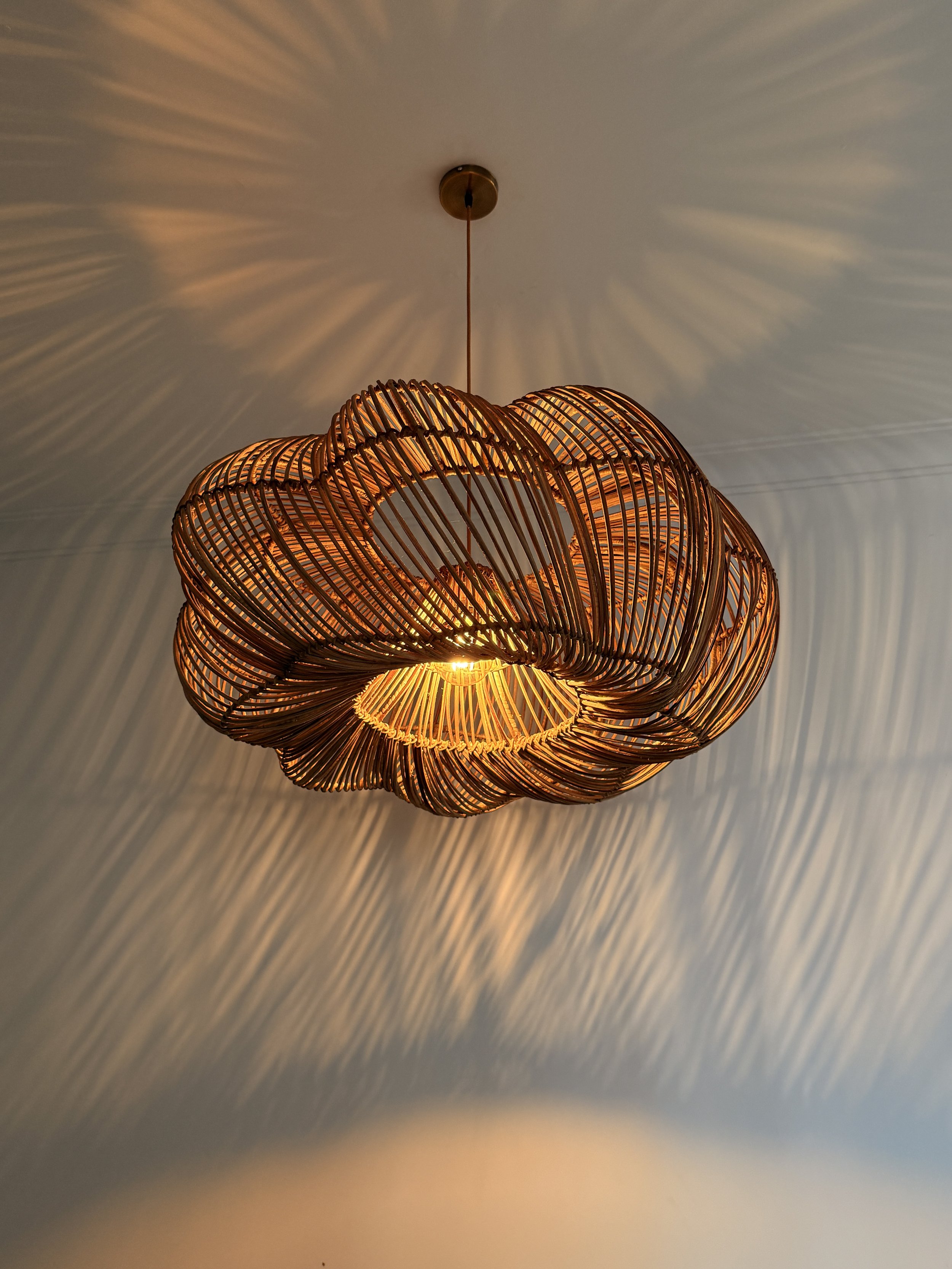 A modern pendant light fixture made of intertwined, ribbed wooden slats hanging from a ceiling, casting decorative shadows.