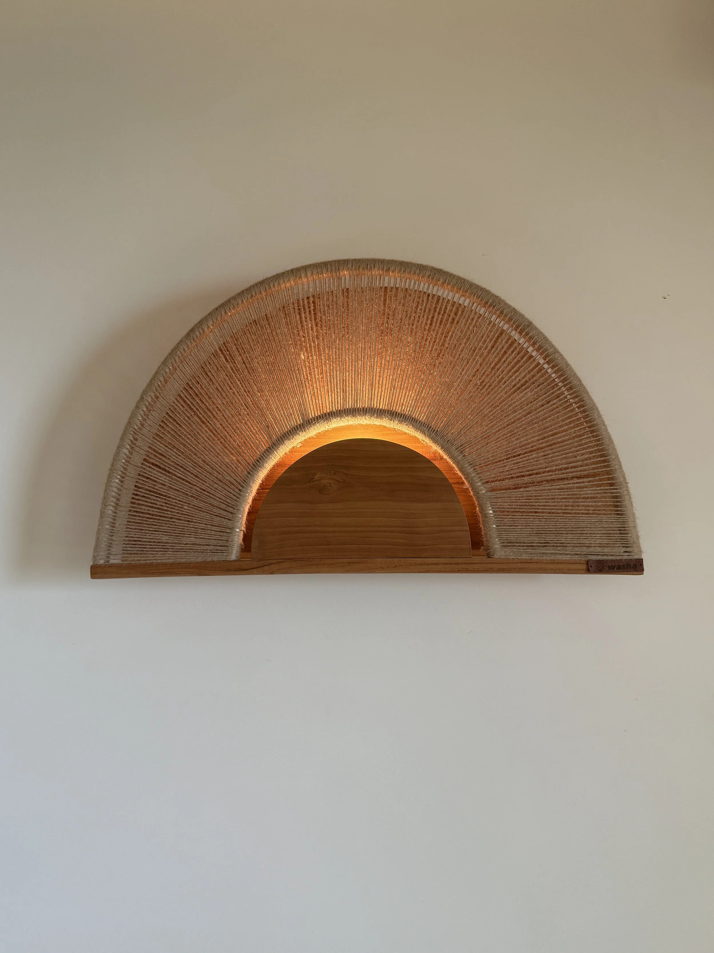 Round wooden mirror with a woven frame and warm backlighting, mounted on a white wall.