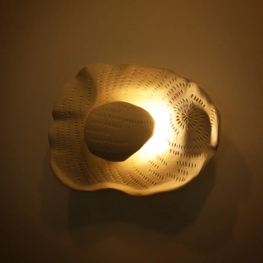A sculptural wall light with flowing, organic curves that creates a gentle, calming glow reminiscent of natural forms.